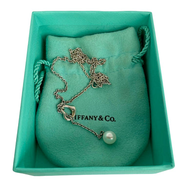 Vintage Tiffany & Co. Elsa Peretti Open Heart sterling silver lariat necklace featuring a sliding open heart pendant and a cultured freshwater pearl on a 19-inch chain, shown in polished pre-owned condition with Tiffany box and pouch.