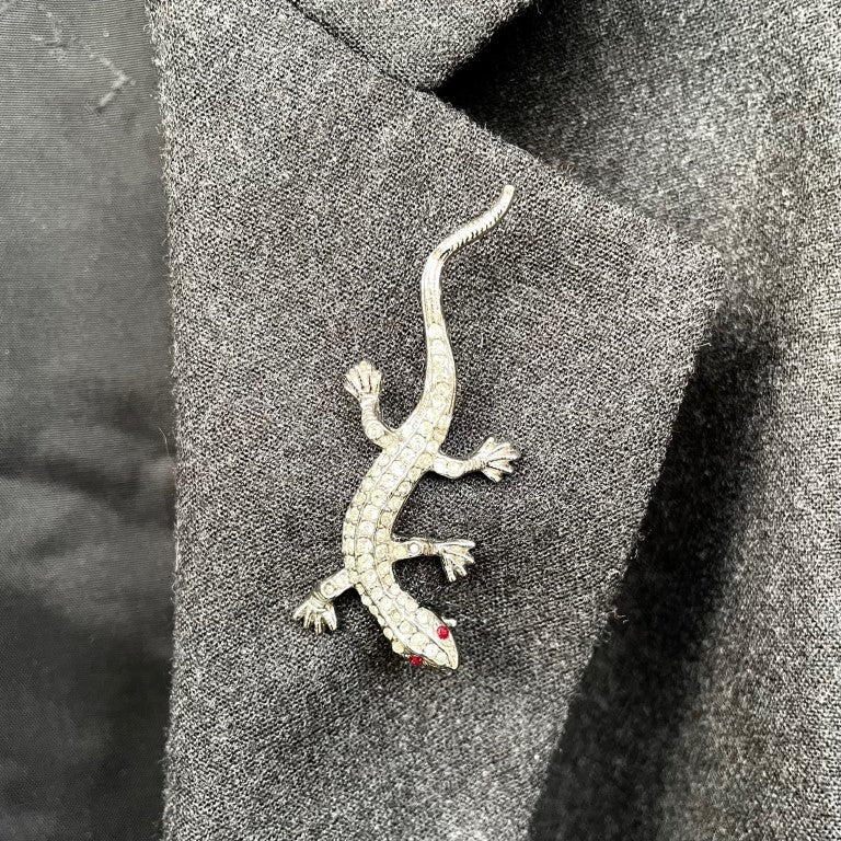 A vintage 1980s Butler & Wilson small lizard brooch entirely pavé set with clear crystals and red crystal eyes shown on a grey suit lapel.