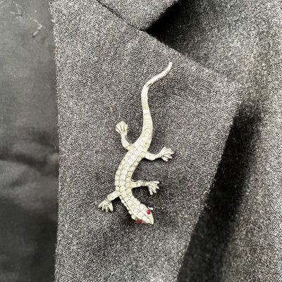 A vintage 1980s Butler & Wilson small lizard brooch entirely pavé set with clear crystals and red crystal eyes shown on a grey suit lapel.
