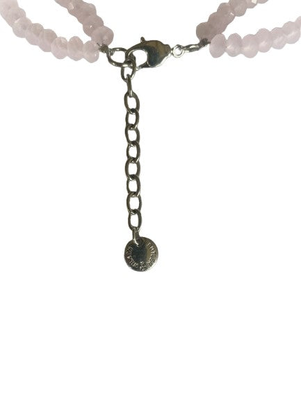 Close-up of silver-tone lobster clasp, extender chain, and signature Butler & Wilson logo tag on a pink beaded necklace with floral centrepiece.
