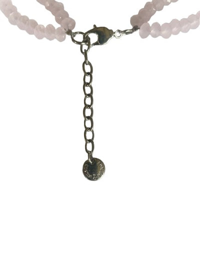 Close-up of silver-tone lobster clasp, extender chain, and signature Butler & Wilson logo tag on a pink beaded necklace with floral centrepiece.
