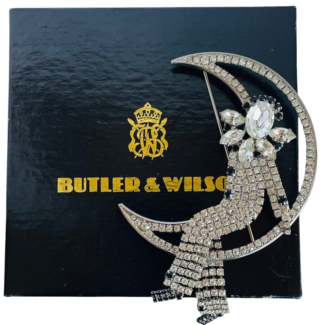 Large vintage 1980s Butler and Wilson crystal Harlequin Pierrot on moon brooch displayed on its black and gold crested gift box.
