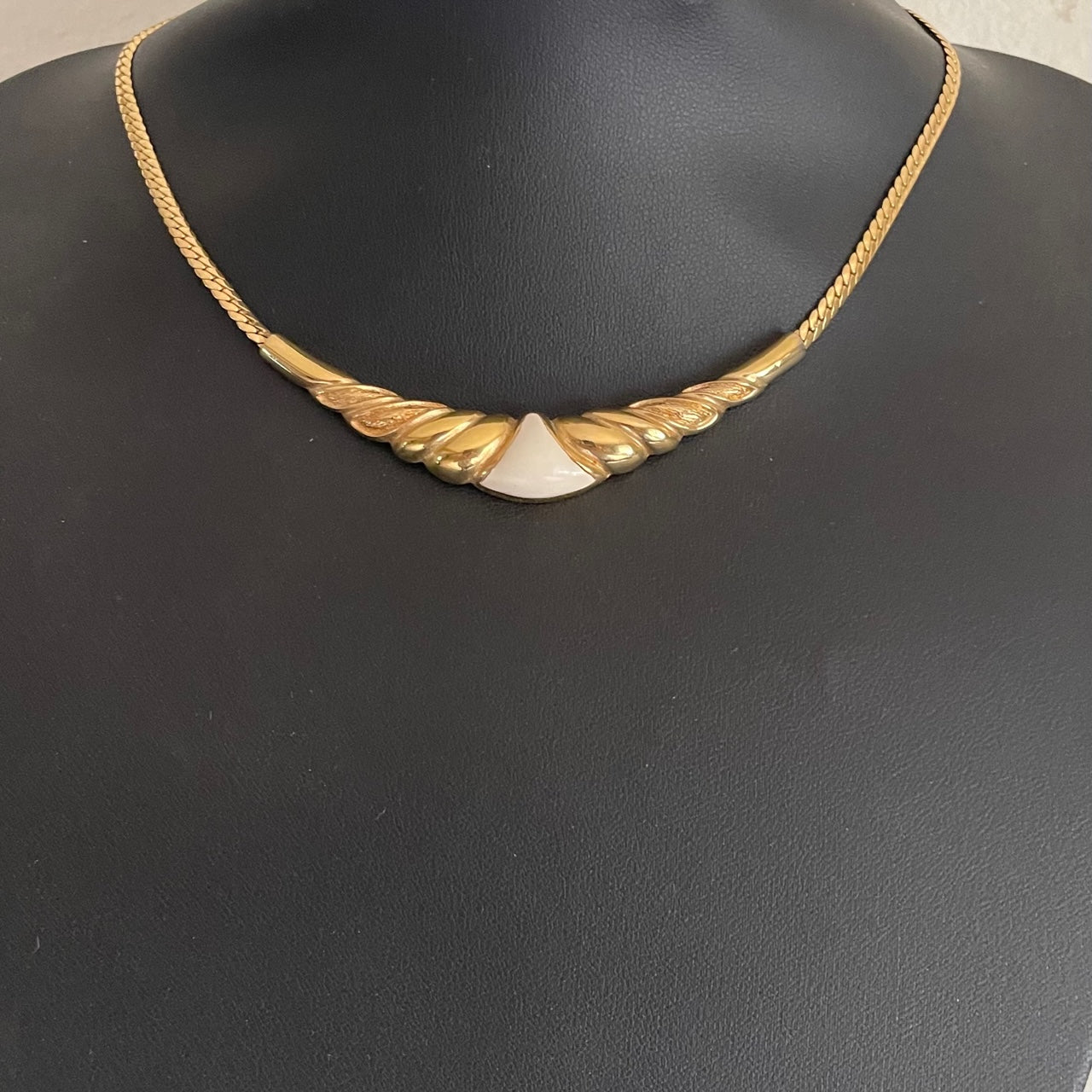 Vintage 1980s Christian Dior gold-plated collar necklace featuring a fluted centerpiece, cream enamel shield insert, and signed CD charm. On black bust. Excellent condition