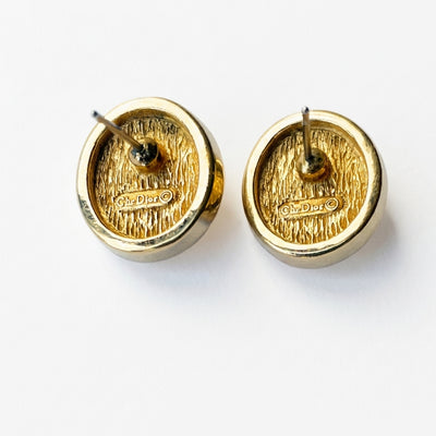 The reverse side of a pair of vintage Christian Dior gold-plated earrings, showing the straight post backings for pierced ears, a textured bark metal finish, and the raised hallmark stamped Chr. Dior ©.
