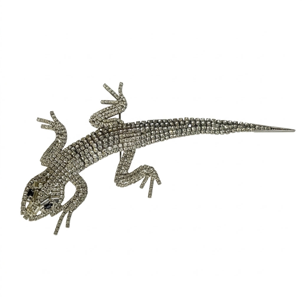 A magnificent 19 cm vintage Butler & Wilson silver-tone articulated lizard brooch encrusted with clear crystals and black eyes, on a white background.