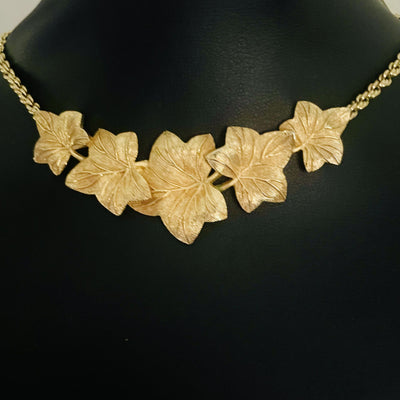 A close-up view of the front of a Christian Dior vintage gold-tone necklace draped over a matte black jewellery display bust. The focus highlights the arrangement of the five overlapping textured ivy leaves, showcasing how they form a gentle V-shape curvature along the neckline.