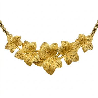A close-up view of the front of a Christian Dior vintage gold-tone necklace on a crisp white background. The focus highlights the arrangement of the five overlapping textured ivy leaves, showcasing how they form a gentle V-shape curvature along the neckline.