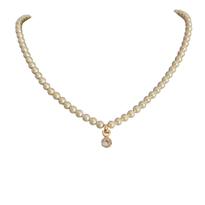 A vintage Christian Dior single-strand cream faux pearl necklace displayed on a white background. The necklace features a central gold-plated pendant drop hanging from a distinct horseshoe-shaped bail, holding a brilliant, bezel-set round clear solitaire crystal.