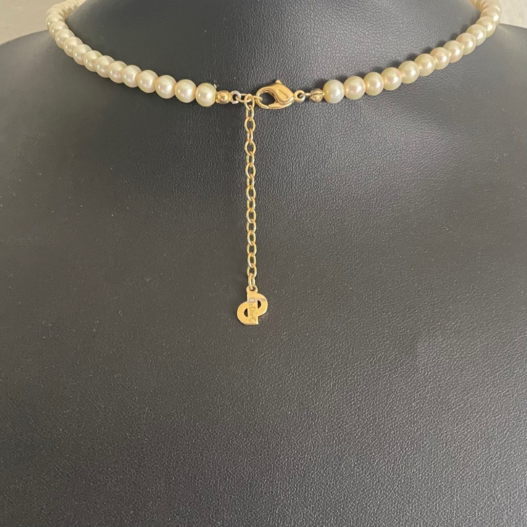 The reverse side of a vintage Christian Dior pearl necklace showing the gold-plated lobster clasp closure and adjustable extender chain. A signature flat gold 'CD' monogram charm hangs from the very end of the extender chain, stamped Chr. Dior ©