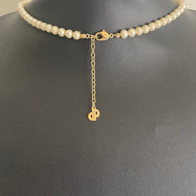 The reverse side of a vintage Christian Dior pearl necklace showing the gold-plated lobster clasp closure and adjustable extender chain. A signature flat gold 'CD' monogram charm hangs from the very end of the extender chain, stamped Chr. Dior ©