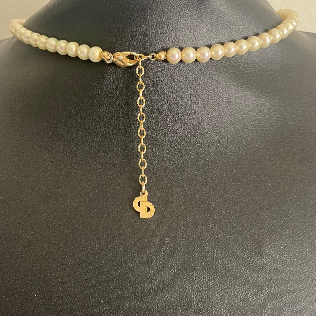 The reverse side of a vintage Christian Dior pearl necklace showing the gold-plated lobster clasp closure and adjustable extender chain. A signature flat gold 'CD' monogram charm hangs from the very end of the extender chain.