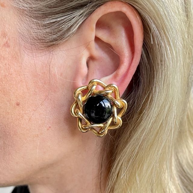Close-up of a model wearing a vintage Christian Dior 1980s gold-plated clip-on earring featuring an onyx-black domed cabochon centerpiece framed by an interwoven chain border.