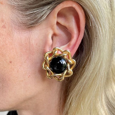 Close-up of a model wearing a vintage Christian Dior 1980s gold-plated clip-on earring featuring an onyx-black domed cabochon centerpiece framed by an interwoven chain border.