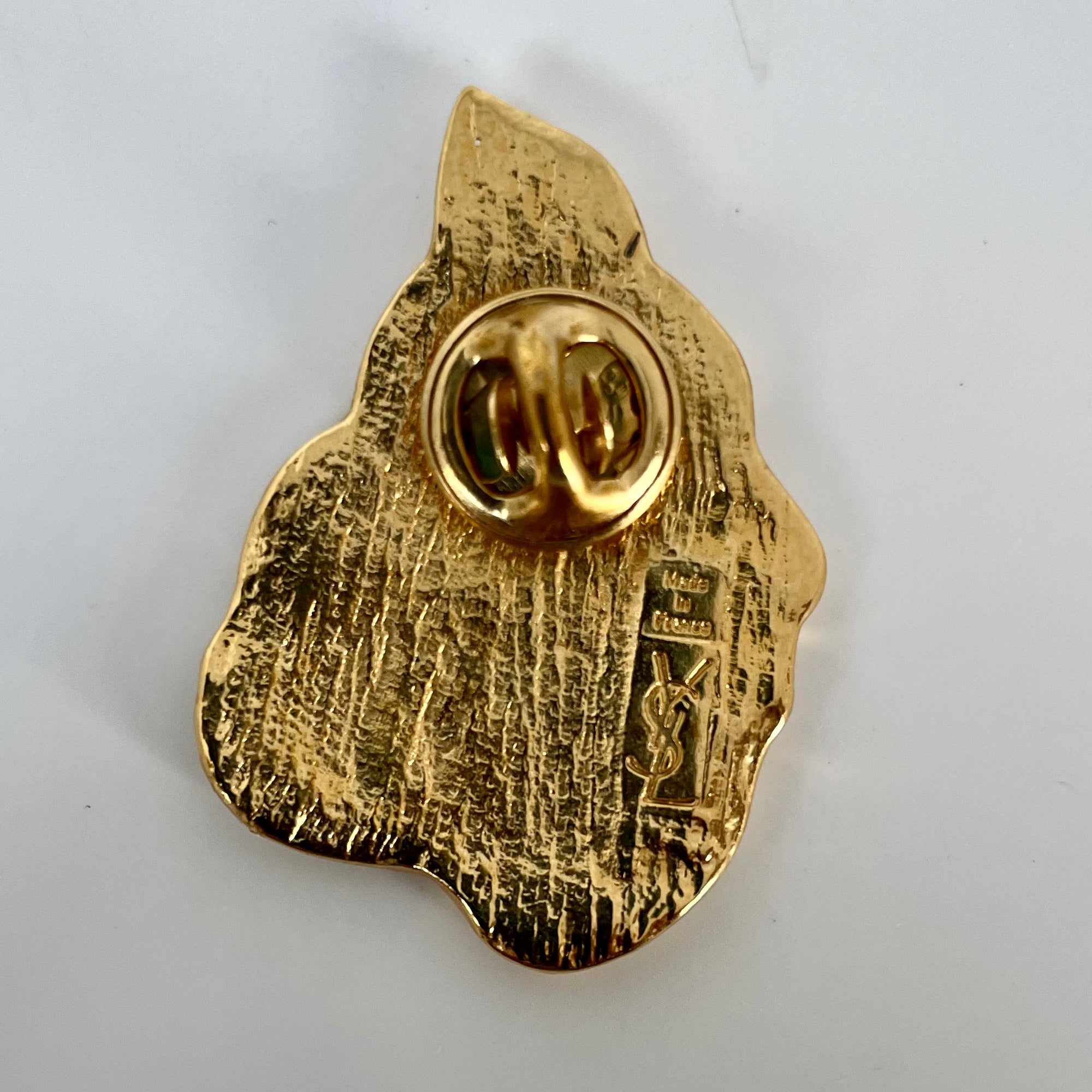 The back of a vintage YSL gold brooch showing a push-on stud closure and an engraved stamp reading Made in France with the vertical YSL logo.