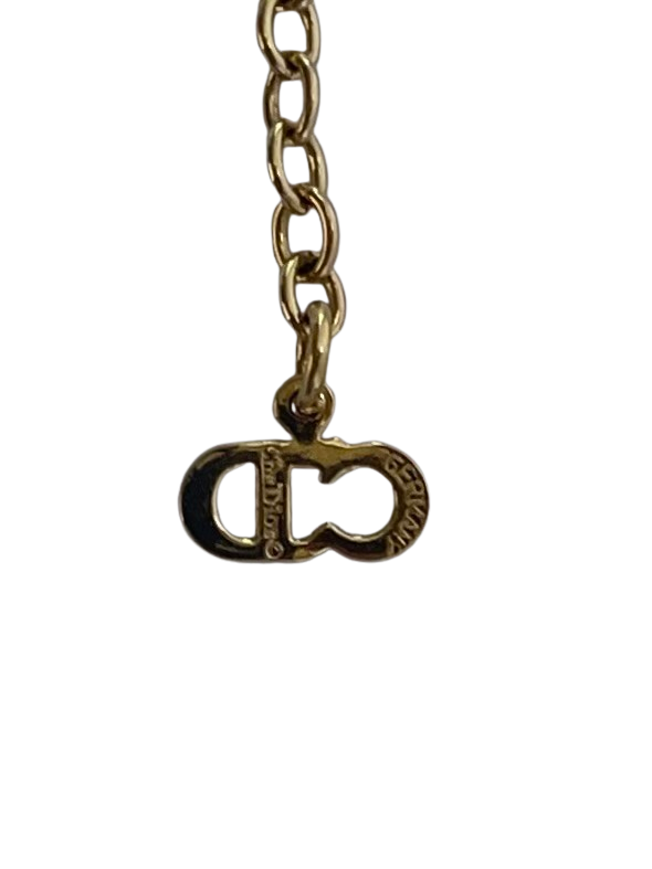 • Macro photograph of the signature "CD" logo charm at the end of a gold-plated extender chain on a vintage Christian Dior necklace. The metal is crisp and engraved clearly with the text "Chr. Dior © GERMANY" across the surface of the letters to prove authenticity.