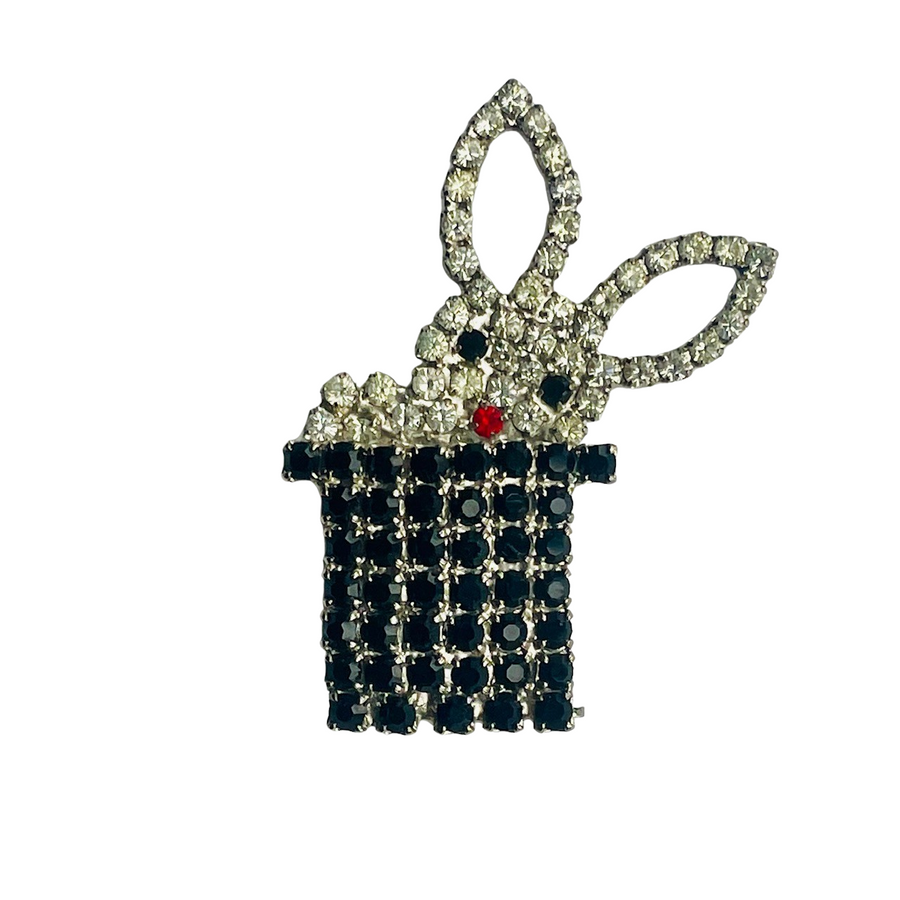 A vintage Butler & Wilson brooch depicting a white rabbit emerging from a top hat, adorned with clear Swarovski crystals, black crystal eyes, and a red crystal nose.